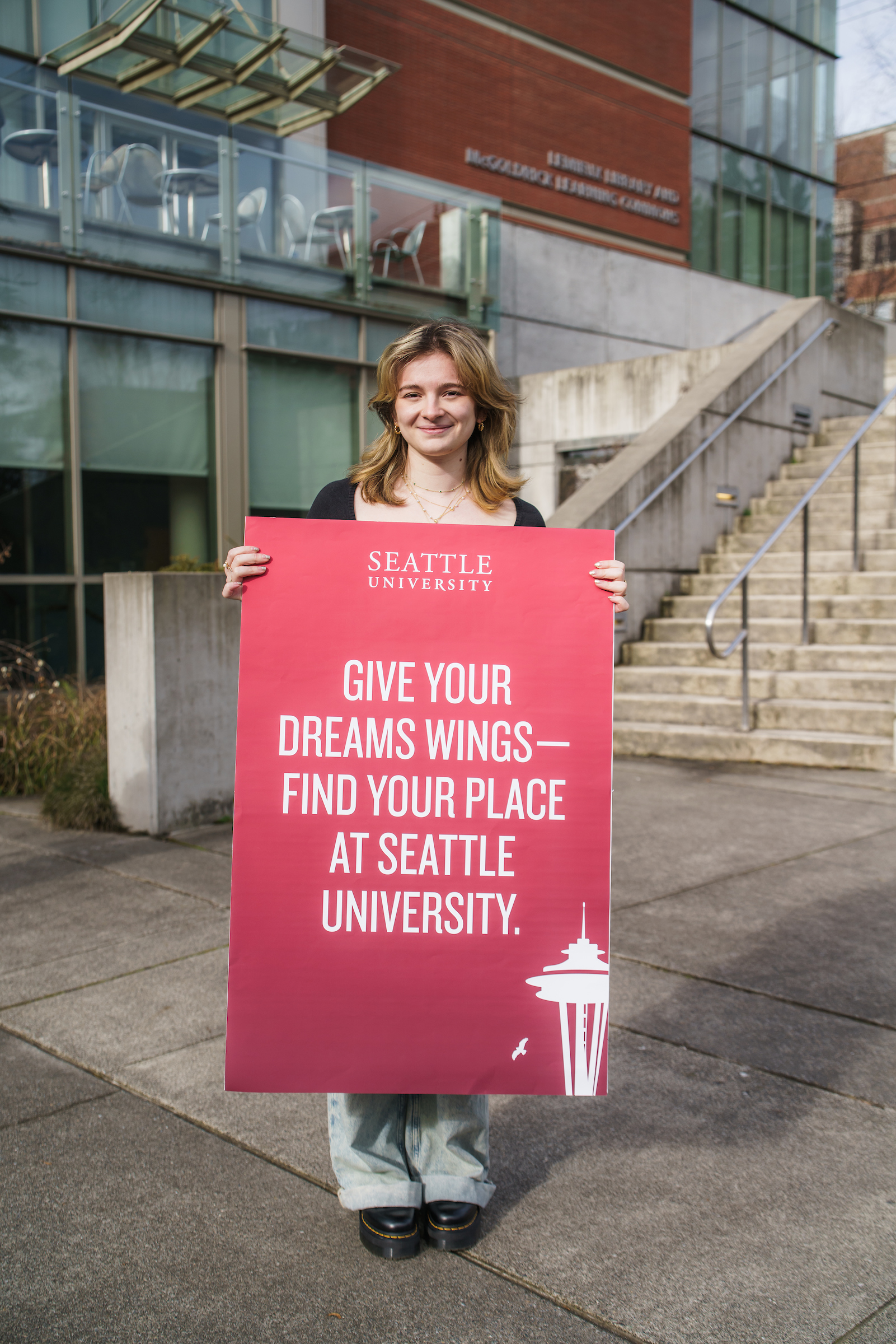 A student holds a poster with the words "GIVE YOUR DREAMS WINGS - FIND YOUR PLACE AT SEATTLE UNIVERSITY"