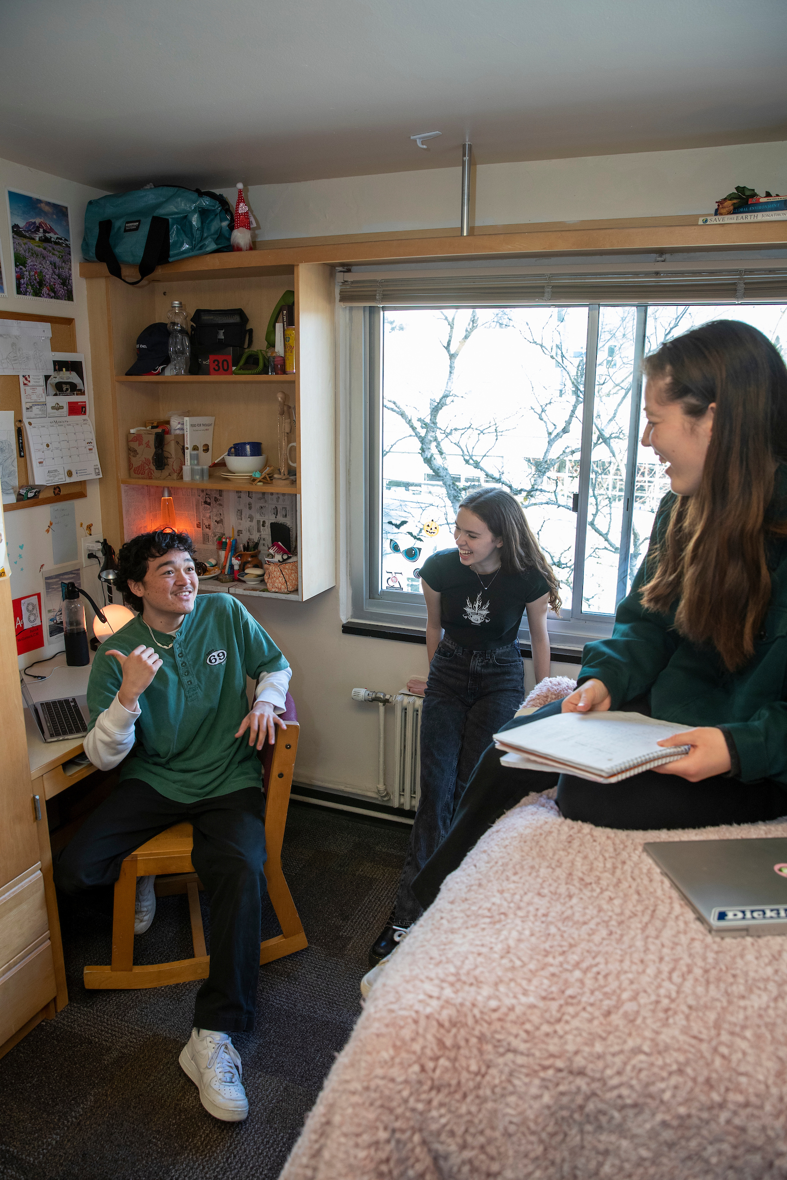 Three students lounge in a residence hall room, laughing.
