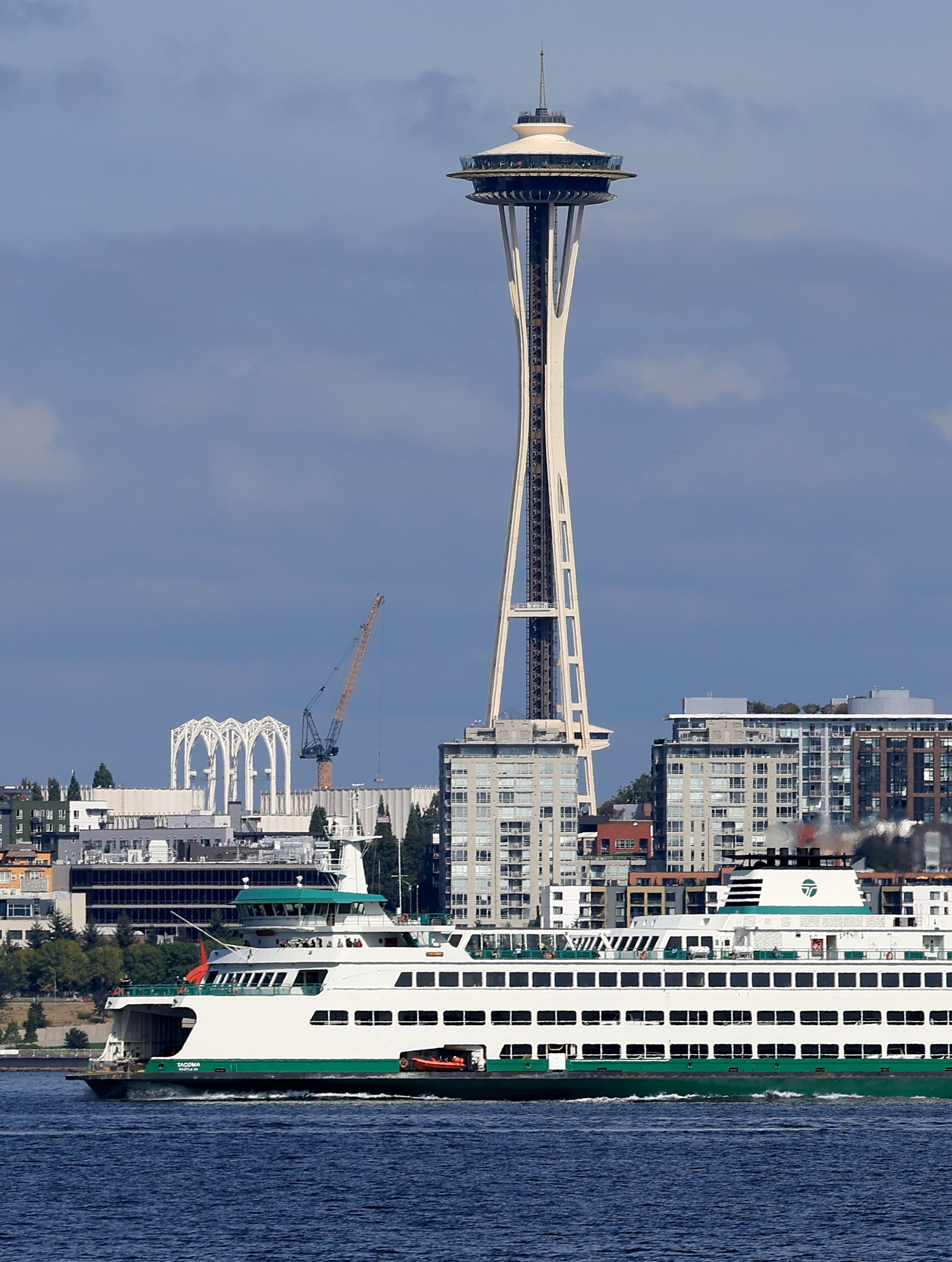 The Space Needle with a blue sky behind it and Elliott Bay and a ferry in the foreground.